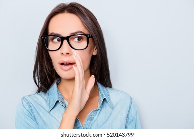 Young woman in glasses holding hand near mouth and telling secret.