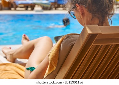 Young woman with glasses uses a smartphone lying on a chaise longue near the pool. Tourism, recreation, relaxation - Powered by Shutterstock