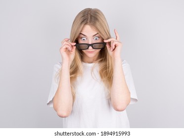 Young woman with glasses is very surprised looking down and lowering her glasses. Surprise and shopping concept on white background.