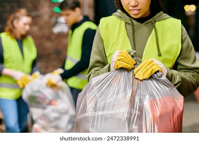 A young woman in gloves and safety vest holding a bag of garbage, recycling with fellow volunteers. - Powered by Shutterstock