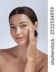 A young woman with glowing skin gently applies skincare to her face, showcasing her healthy, radiant complexion. Ideal for beauty, skincare, and self-care promotions, highlighting facial care and