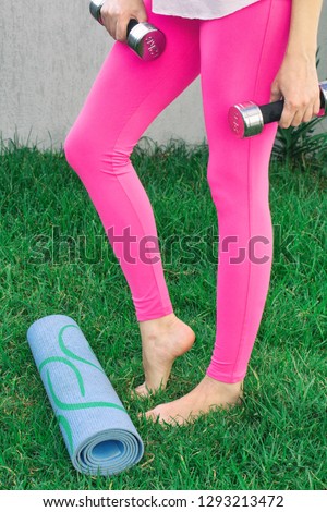 Young woman goes in for sports. Female legs playing sports in nature with dumbbells.