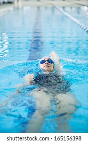 Young Woman In Goggles And Cap Swimming Back Crawl Stroke Style In The Blue Water Indoor Race Pool