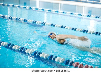 Young Woman In Goggles And Cap Swimming Front Crawl Stroke Style In The Blue Water Indoor Race Pool