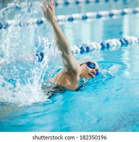 Young woman in goggles and cap swimming front crawl stroke style in the blue water indoor race pool - Powered by Shutterstock