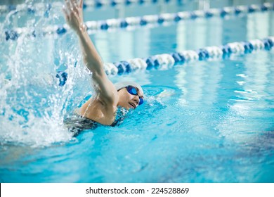 Young Woman In Goggles And Cap Swimming Front Crawl Stroke Style In The Blue Water Indoor Race Pool