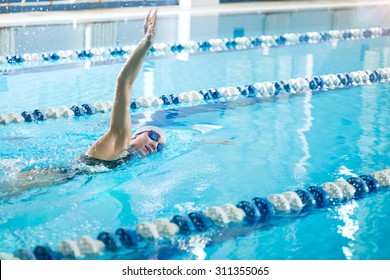 Young woman in goggles and cap swimming front crawl stroke style in the blue water indoor race pool - Powered by Shutterstock