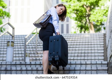 young woman going up the stairs with suitcase. back view.