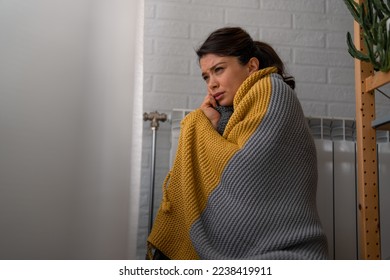 A young woman is going through an energy crisis and feeling cold in the apartment. Woman is feeling cold at home because of an energetic crisis and trying to warm herself up near the radiator.
