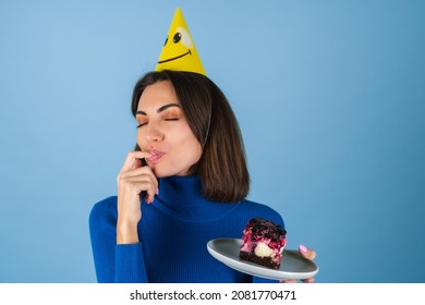 Young Woman In Golf On A Blue Background Celebrates A Birthday, Holds A Piece Of Cake, Happy, Licks Her Finger With Pleasure