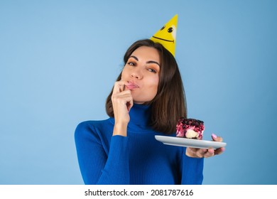 Young Woman In Golf On A Blue Background Celebrates A Birthday, Holds A Piece Of Cake, Happy, Licks Her Finger With Pleasure