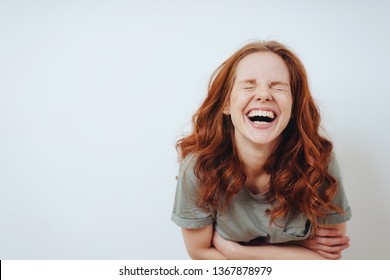 Young woman with a good sense of humor enjoying a laugh screwing up her eyes in amusement over white with copy space - Shutterstock ID 1367878979