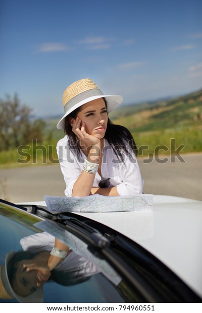 Young woman got lost in the field while driving a car\
and reading paper map