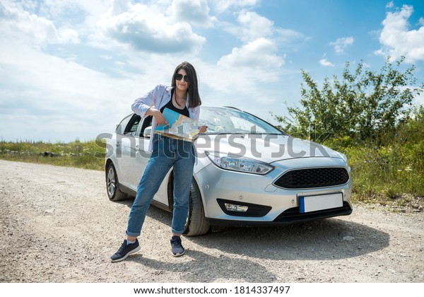 Young woman got lost and\
looking to a map for planning new trip. Lady standing in road  near\
car