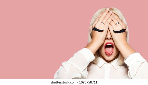 Young Woman With Gray And Black Eyelashes Painted On Hands. Blonde Hair Girl Closed Her Eyes With Hands And Shout. Portrait Of Surprised Model In White Shirt. Concept Of Fun And Tomfoolery.