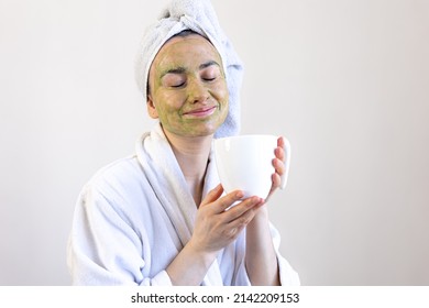 Young Woman With A Green Beauty Mask On Her Face And With A Cup.