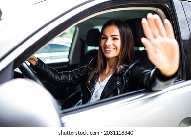 Young woman greeting with hand from car. Cheerful caucasian girl welcome somebody sitting in automobile - Shutterstock ID 2031118340