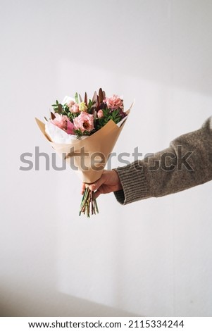 Young woman in grey knitted sweater with bouqet of flowers in hand on the grey background
