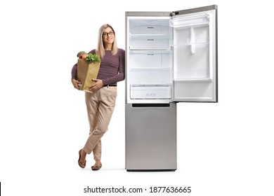 Young woman with a grocery bag leaning on an empty fridge with an open door isolated on white background