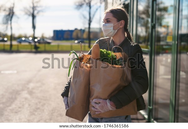A young woman\
with grocery bags from a supermarket. Social distancing: face mask,\
disposable gloves to prevent infection and epidemic. Food shopping\
during quarantine