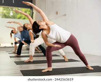 Young woman with group of active different ages women exercising and making extended side sngle pose during yoga classes in modern sports gym - Powered by Shutterstock