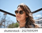 young woman with hair in the wind wearing sunglasses on a sunny day