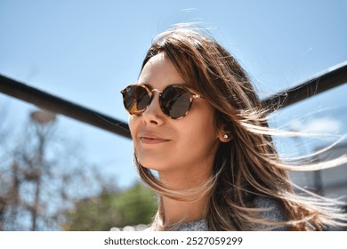 young woman with hair in the wind wearing sunglasses on a sunny day - Powered by Shutterstock