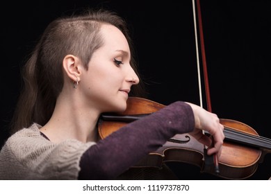 Young Woman With Half Of Her Hair Shaved While Playing A Baroque Violin On A Black Background