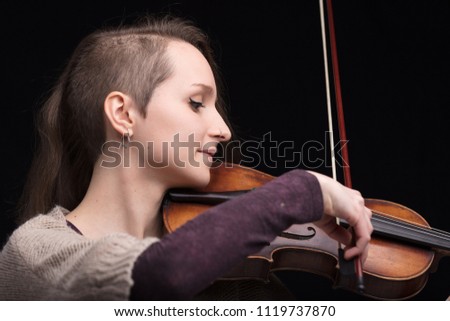 young woman with half of her hair shaved while playing a baroque violin on a black background
