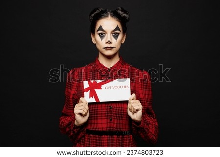 Young woman with Halloween makeup face art mask wear clown costume red dress hold store gift coupon voucher card isolated on plain solid black background studio portrait. Scary holiday party concept