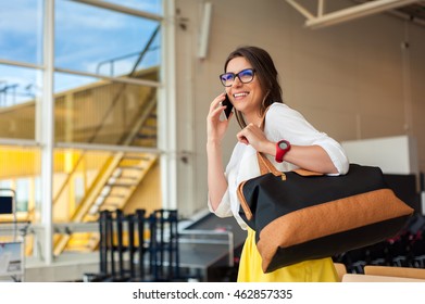 Young Woman With A Hand Bag In Casual Wear Holding His Luggage While Sitting In The Hall Of The Airport Waiting For His Flight.