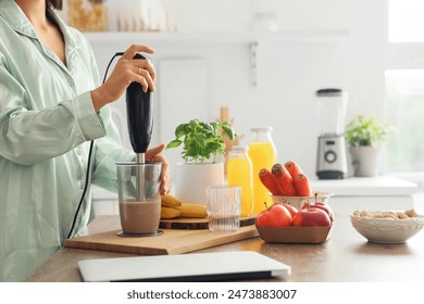 Young woman with hand blender making smoothie for breakfast in kitchen, closeup - Powered by Shutterstock