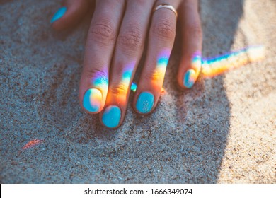 Young woman hand with blue manicure and reflection of rainbow on sand, close-up. - Powered by Shutterstock