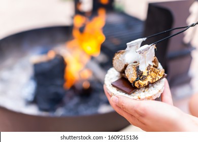 Young Woman Hand Holding Gooey Roasted Charred Marshmallows Smores With Chocolate And Rice Cake Cracker By Fire In Campground Campfire Grill