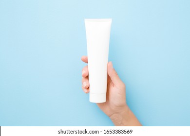 Young Woman Hand Holding And Showing White Tube On Light Blue Background. Pastel Color. Care About Clean And Soft Body Skin. Daily Beauty Product. Closeup. 