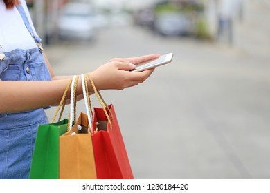 young woman hand holding smartphone and shopping bags with standing at the car parking lot