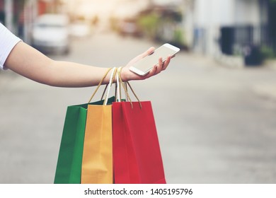 young woman hand holding smartphone and shopping bags with standing at the car parking lot