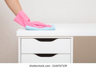Young woman hand in pink rubber protective glove holding blue dry rag and wiping dust from white work table with drawers at home office. Closeup. General or regular cleanup in room. Cleaning service. - Shutterstock ID 2144767139