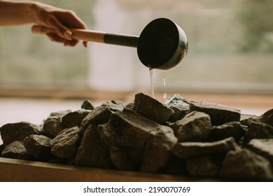 Young woman hand pouring water on hot rocks in the sauna
