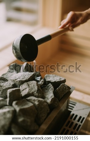 Young woman hand pouring water on hot rocks in the sauna