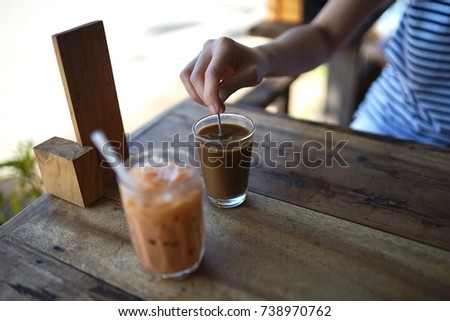 Young woman hand and spoon with Traditional Thai hot coffee and iced milk tea