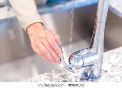 Young Woman Hand Turning On Faucet In Modern Kitchen With Granite Countertops Closeup Showing Stainless Steel Luxury Sink