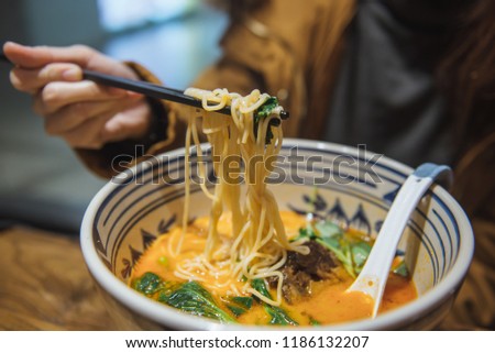 Young woman hand uses chopsticks to pickup tasty noodles delicious chinese ramen with pork and vegetarian soup with turmeric.