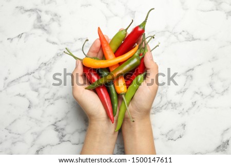 Young woman with handful of different hot chili peppers at marble table, top view