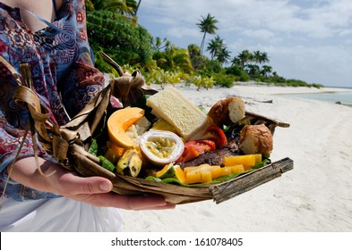 Young Woman Hands Carry Tropical Food Of Grilled Fish, Fruits And Vegetables Dish Served On Deserted Tropical Island In Aitutaki Lagoon, Cook Islands.