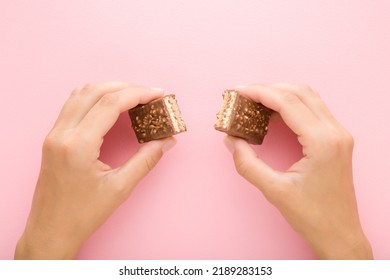 Young Woman Hands Holding Broken Dark Brown Chocolate Bar With Nuts On Light Pink Table Background. Pastel Color. Sweet Snack. Two Pieces. Closeup. Point Of View Shot. 