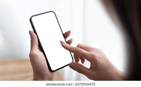 Young woman hands holding cell phone touching finger on mockup white blank display, empty screen for social media app ad at home. Mobile application tech concept, over shoulder view, closeup