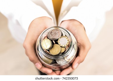 Young Woman Hands Holding Glass Jar With Multi Currency Coins Inside, Top View â?? Money Saving And Financial Concept