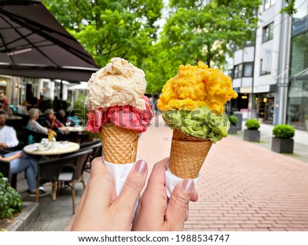 Young woman hands holding ice cream cones on summer day in the city. Tasty colorful fruit and berry ice cream