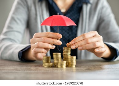 Young woman hands holding red umbrella over stacked coin on table. Female hand holding a small umbrella to protect heaps of coins while saving them. Financial security and savings protection concept.